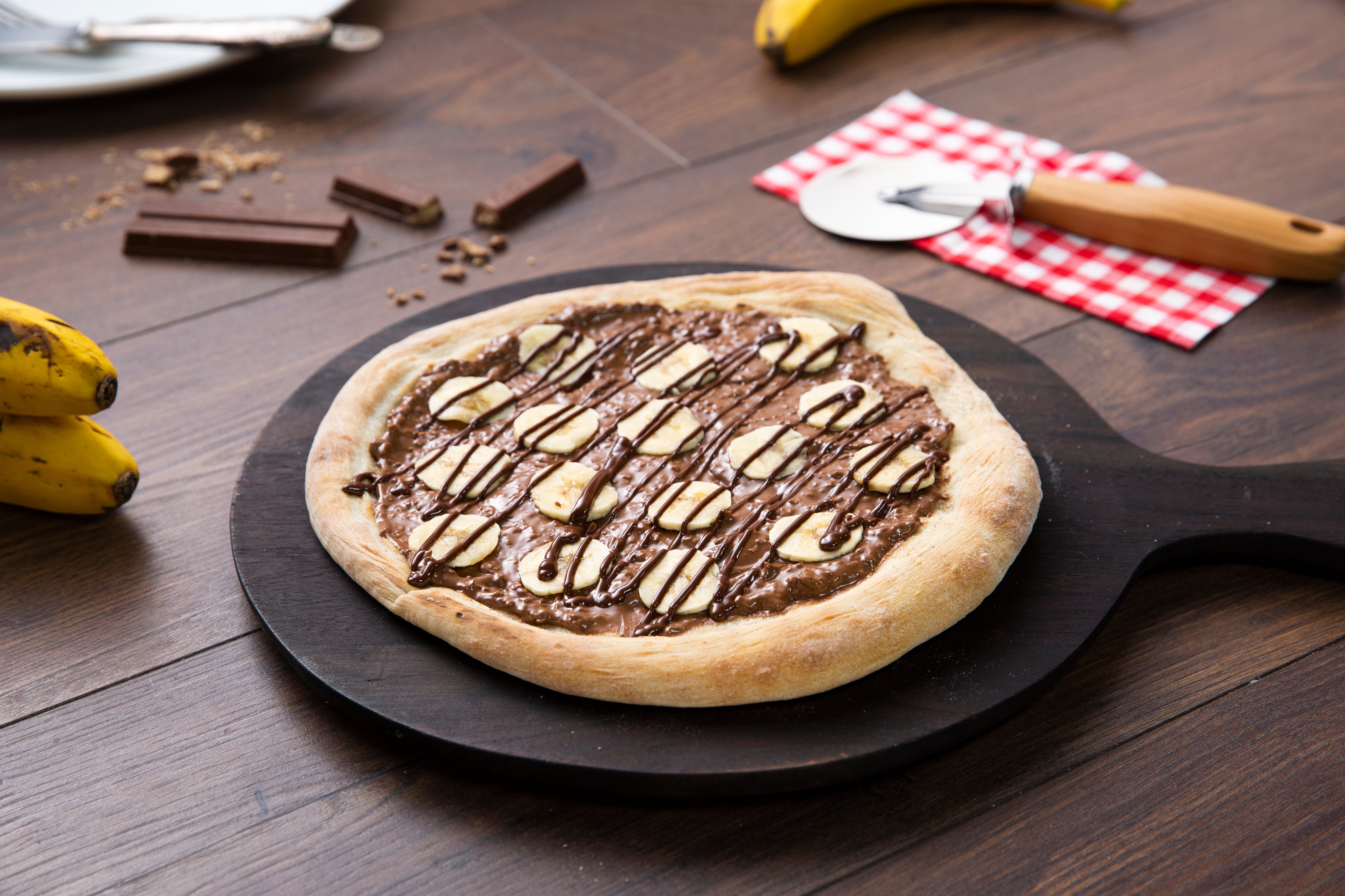 Una pizza dulce con KITKAT® untable, trozos de banano y chocolate derretido