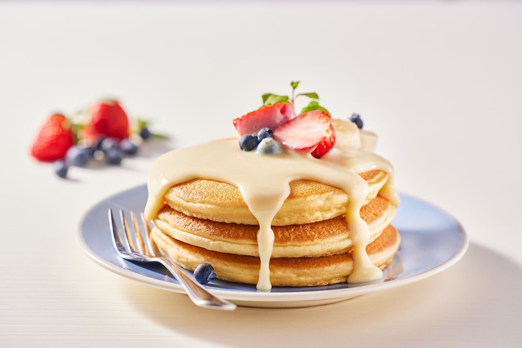 Panqueques con crema, cubiertos con fresas y arándanos, hecho posible por un proveedor de lácteos al por mayor