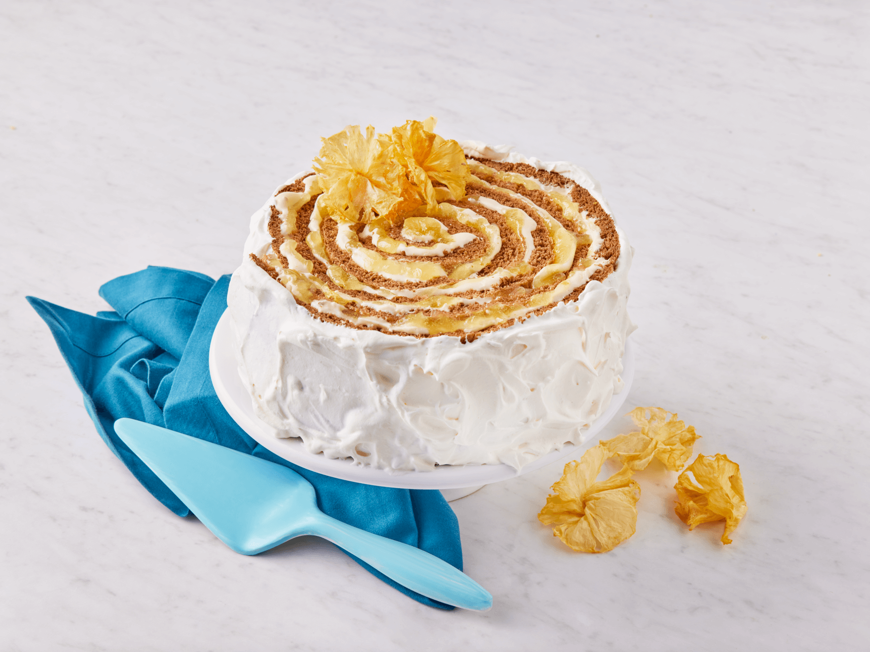 Pastel redondo con diseño en espiral, glaseado blanco y piña seca de NESTLÉ® foodservice, colocado sobre un paño azul.