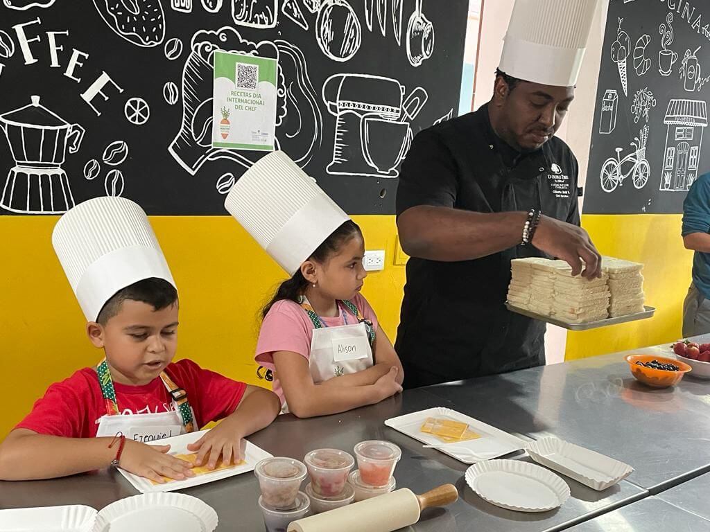 Chef repartiendo ingredientes a niños para iniciar el taller de consumo de frutas y verduras