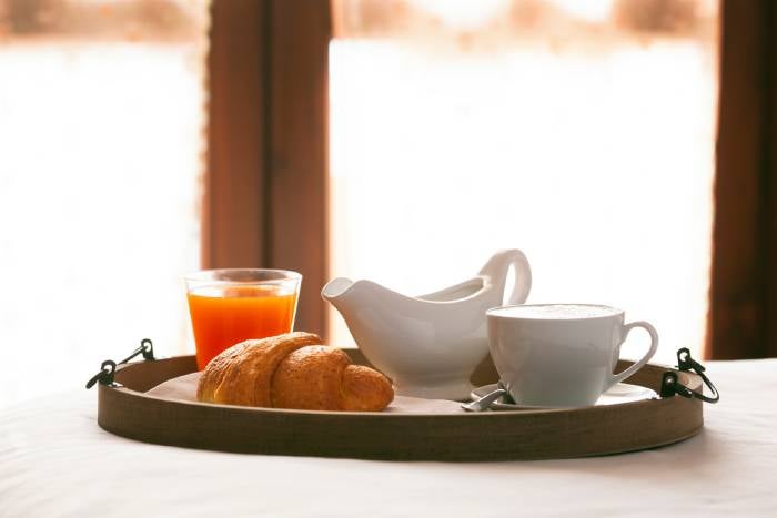 Desayuno de café con croissant y jugo de naranja sobre bandeja de madera