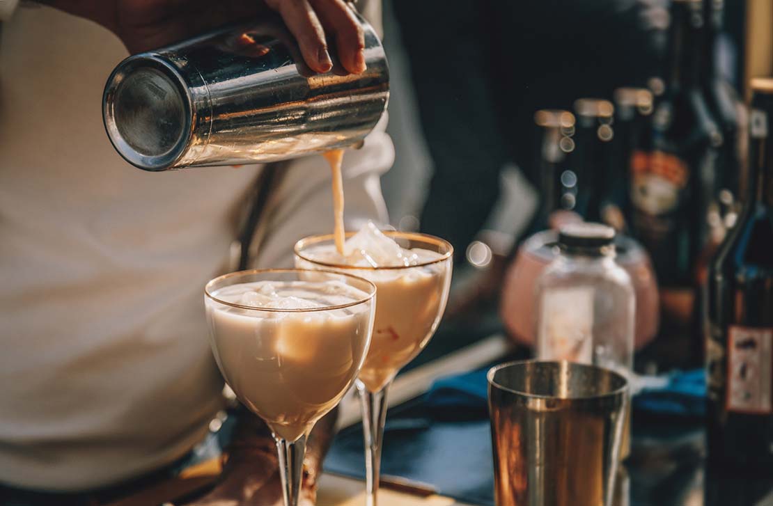 Sobre una mesa con botellas, un barista prepara dos cocteles de café para la cena de fin de año