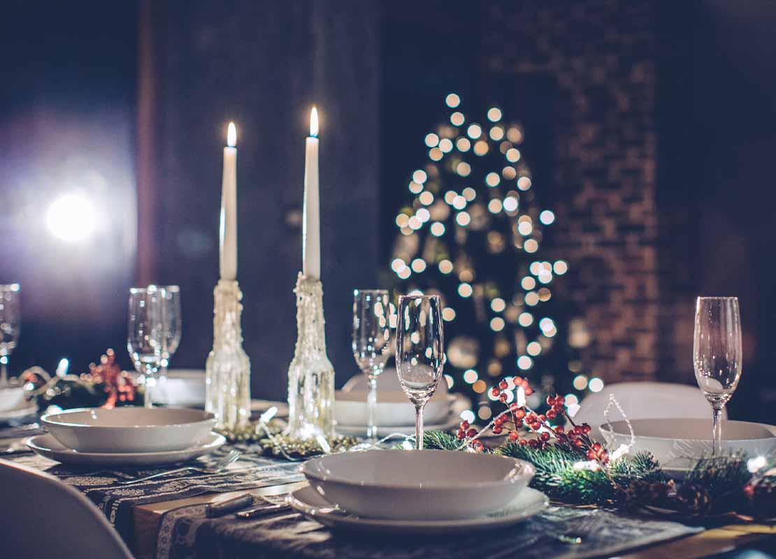 Mesa preparada para la cena de fin de año con velas, servicio para varias personas y árbol de Navidad al fondo