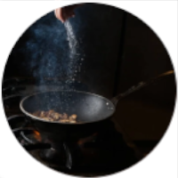 Mano agregando sal a una sartén que esta sobre el fuego