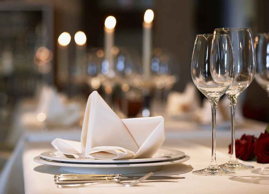 Servilleta sobre plato acompañado de copas y cubiertos sobre la mesa de un restaurante para cena de fin de año