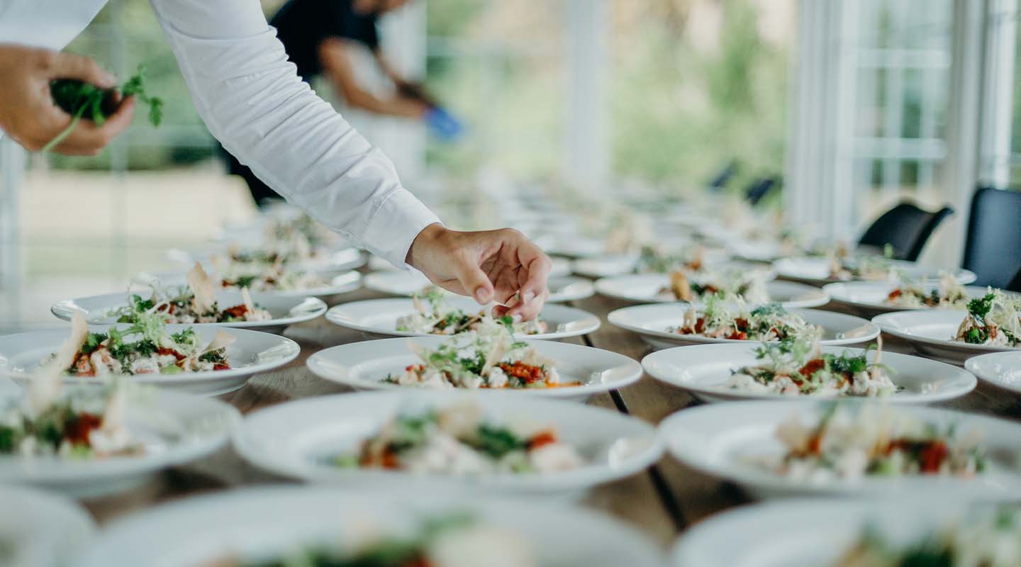 Personal capacitado sirve y decora varios platos ubicados ordenadamente en una mesa para un servicio de catering