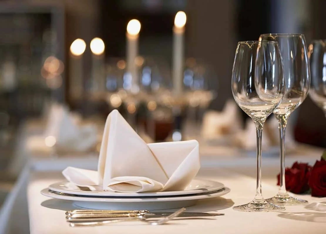 Servilleta sobre plato acompañado de copas y cubiertos sobre la mesa de un restaurante para cena de fin de año