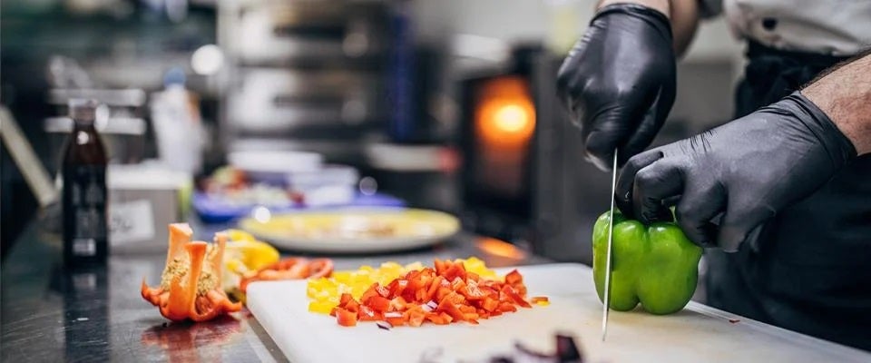 Un chef está cortando un pimiento morrón verde en una tabla de cortar en una cocina