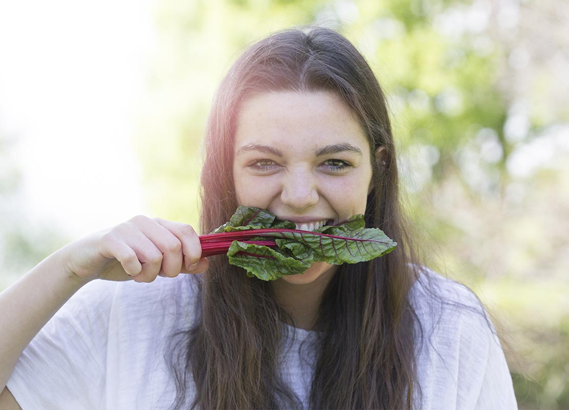 Mujer mordiendo hojas de acelga roja