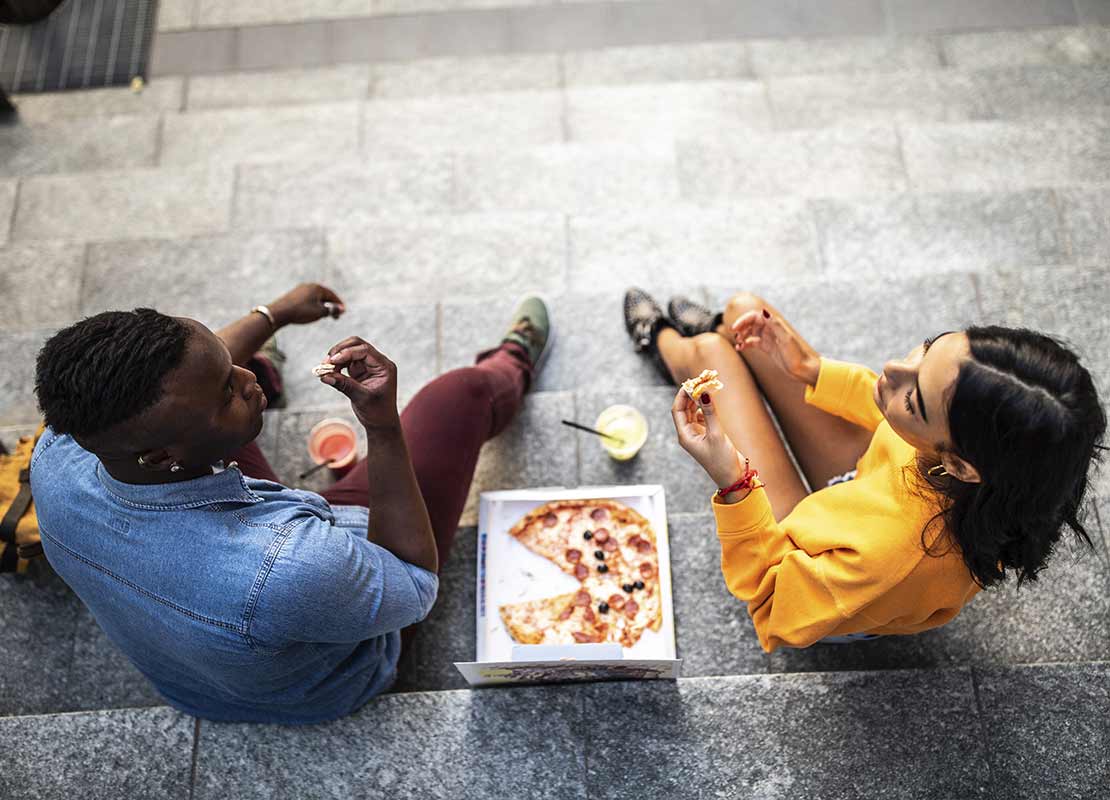 Pareja de Millennials sentados en unas escaleras disfrutando de una pizza juntos