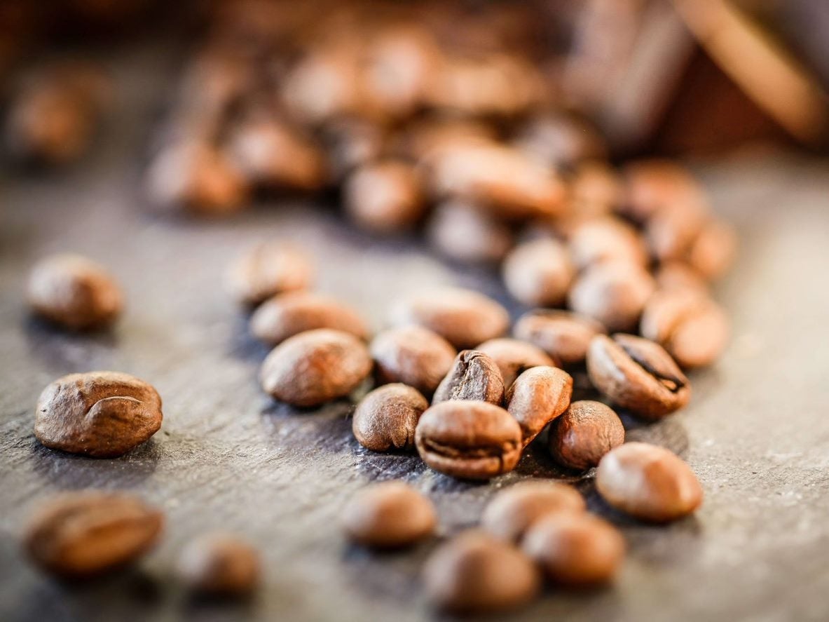 Granos de café tostados, uno de los insumos esenciales para las máquinas de café, esparcidos sobre una mesa.