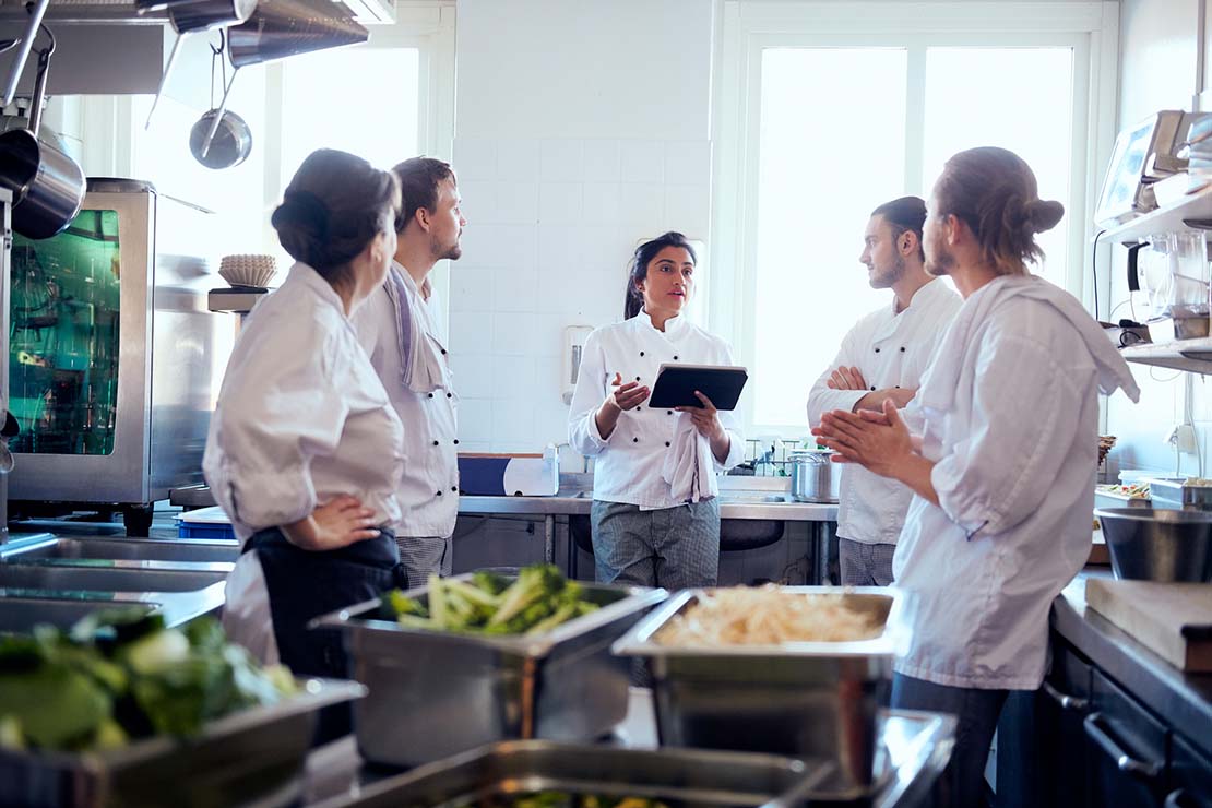 En una cocina industrial, la chef ejecutiva incentiva al personal a continuar con su formación profesional