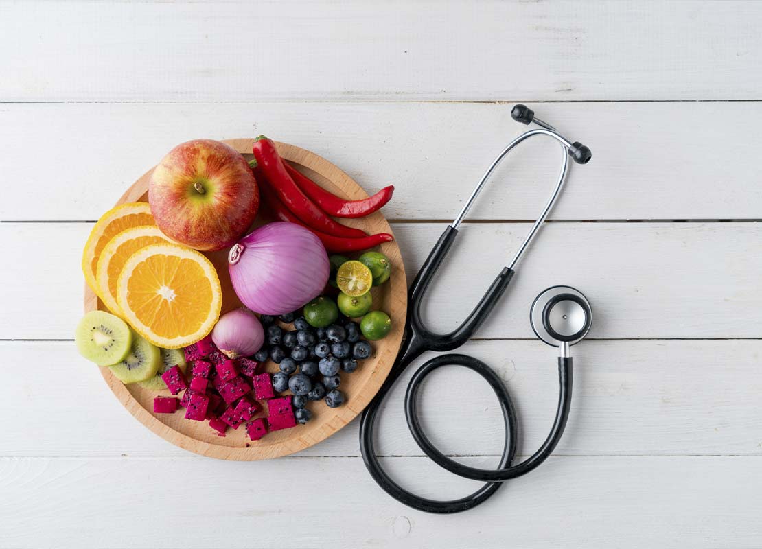 Plato de madera con frutas y verduras junto a un estetoscopio