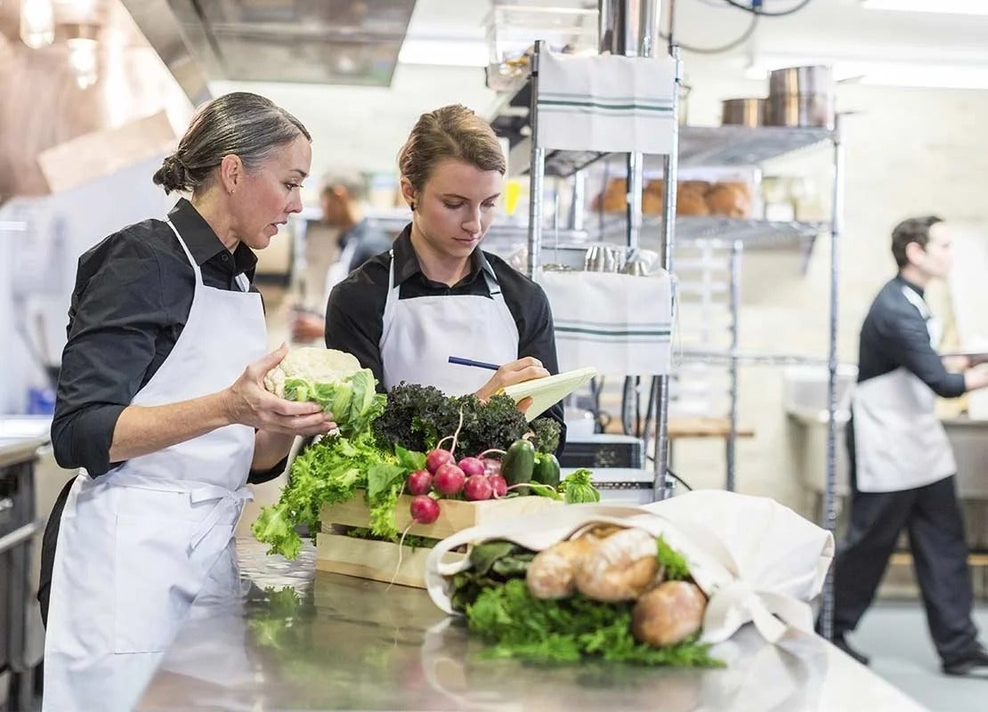 Chefs con delantales blancos revisando e inventariando las verduras que llegan a su restaurante