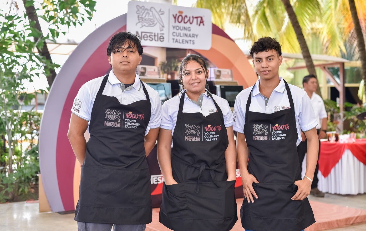 Tres jóvenes con delantales posan juntos, representando el programa YOCUTA de Nestlé