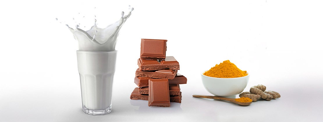 Vaso de leche con splash, barra de chocolate en trozos, taza y cuchara de madera con una especia en polvo