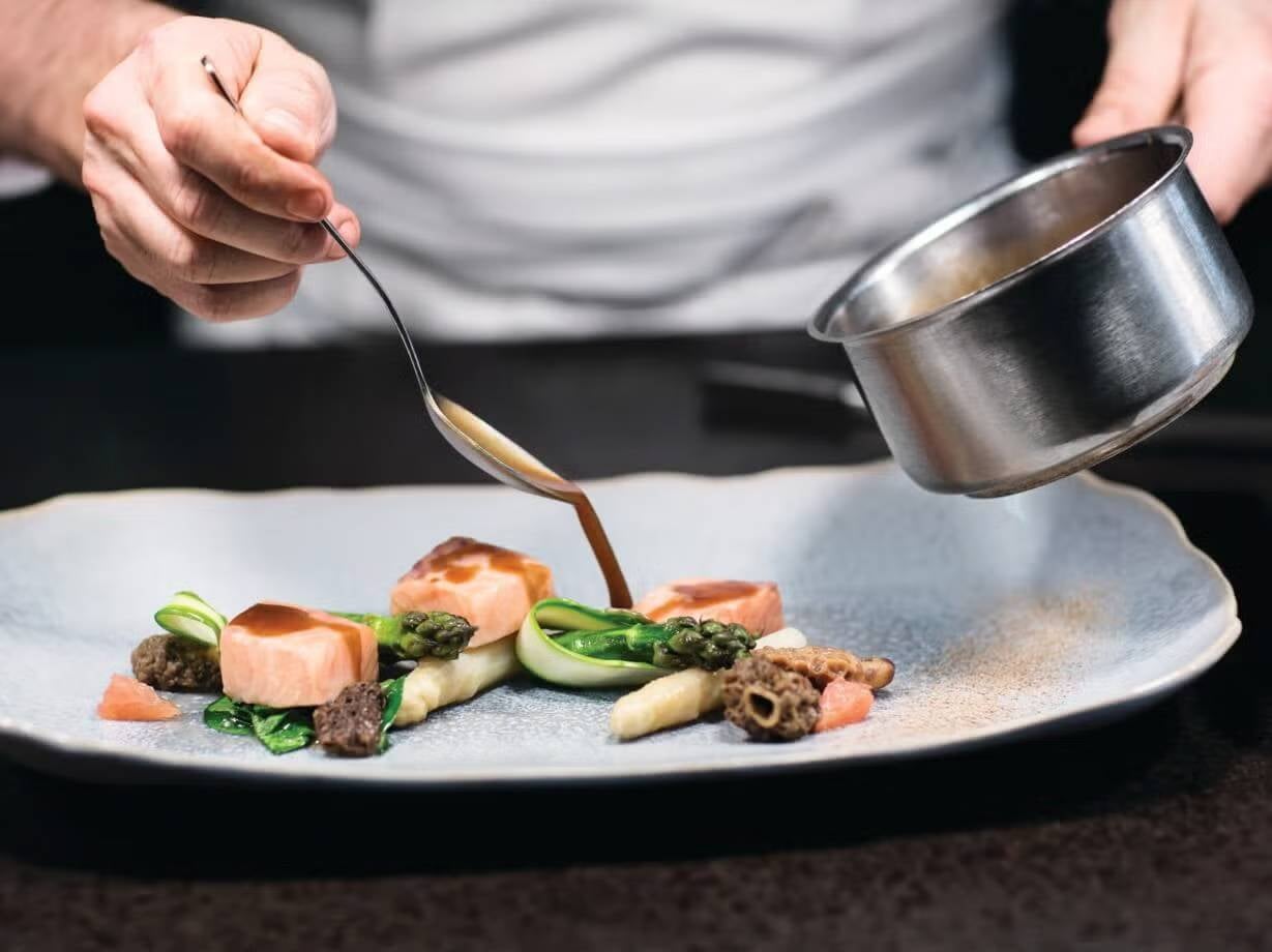 Manos de chef vierten salsa con una cuchara sobre una de las recetas para negocios de NESTLÉ PROFESSIONAL®