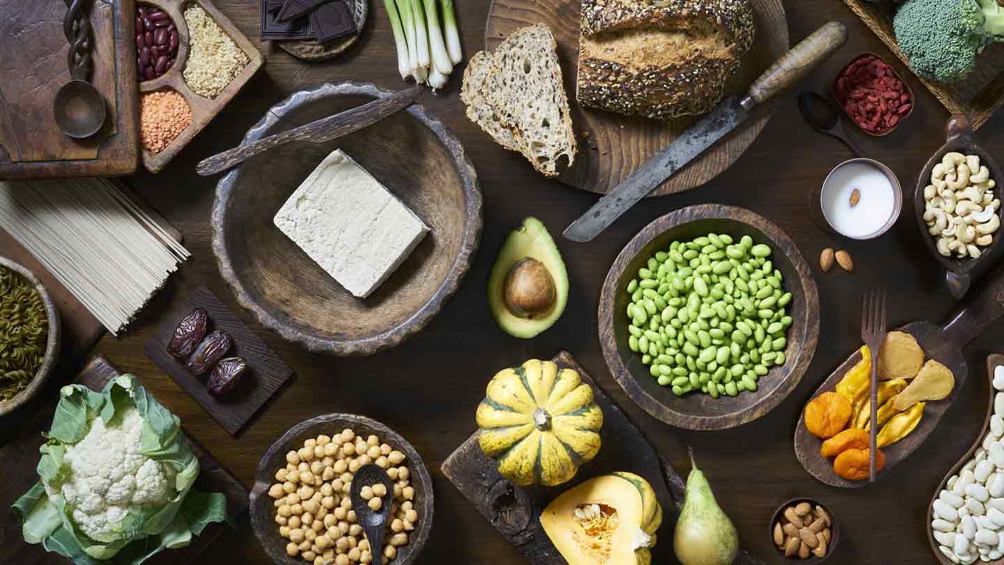 Verduras, frutas, legumbres, cereales y otros alimentos de origen vegetal en una mesa de madera