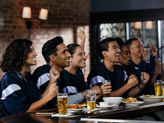 Grupo de amigos festejan sentados en la barra de un gastrobar donde hay comida y bebidas