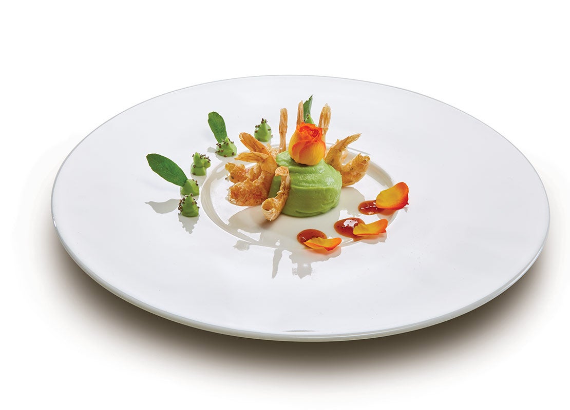 Camarones en tempura, mousse verde y pétalos comestibles presentado en el centro de un plato grande