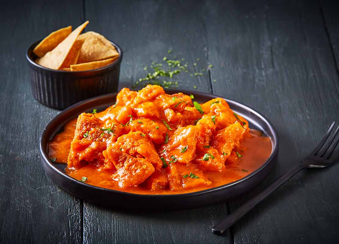 Plato de chicharrón en salsa roja que llega al borde y hierbas frescas, acompañado de totopos