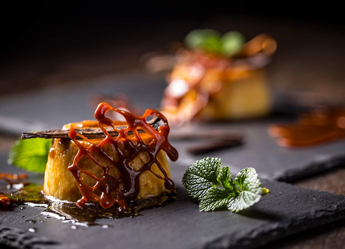 Postre tipo flan, decorado con caramelo y hojas de menta, servido sobre una pizarra negra