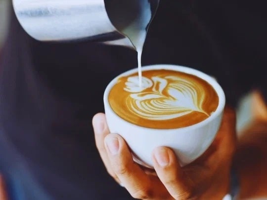 Taza de café con latte art en manos de una persona profesional