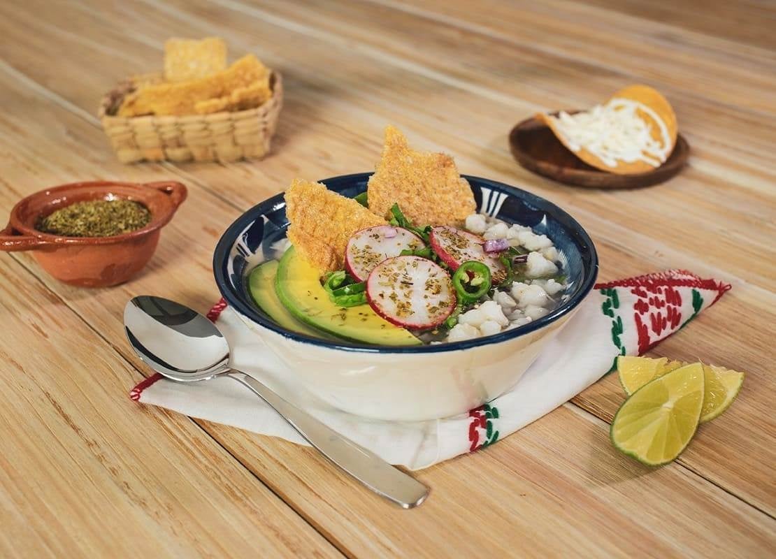 Pozole blanco con aguacate, rábanos y tostadas, acompañado de limón, orégano y queso