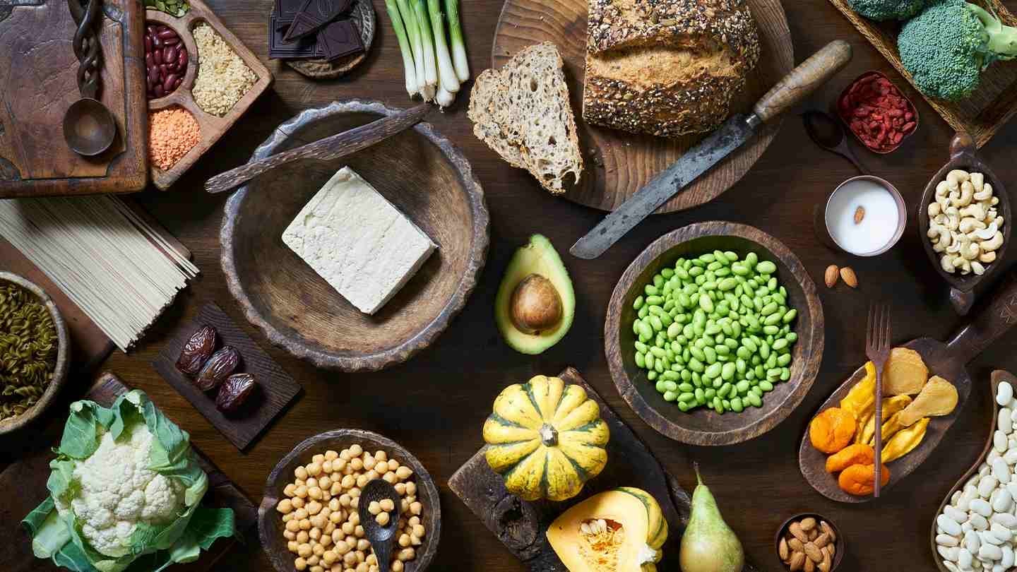 Diversos alimentos en recipientes de madera como frutas, verduras, tofu, frutos secos, cereales, entre otros