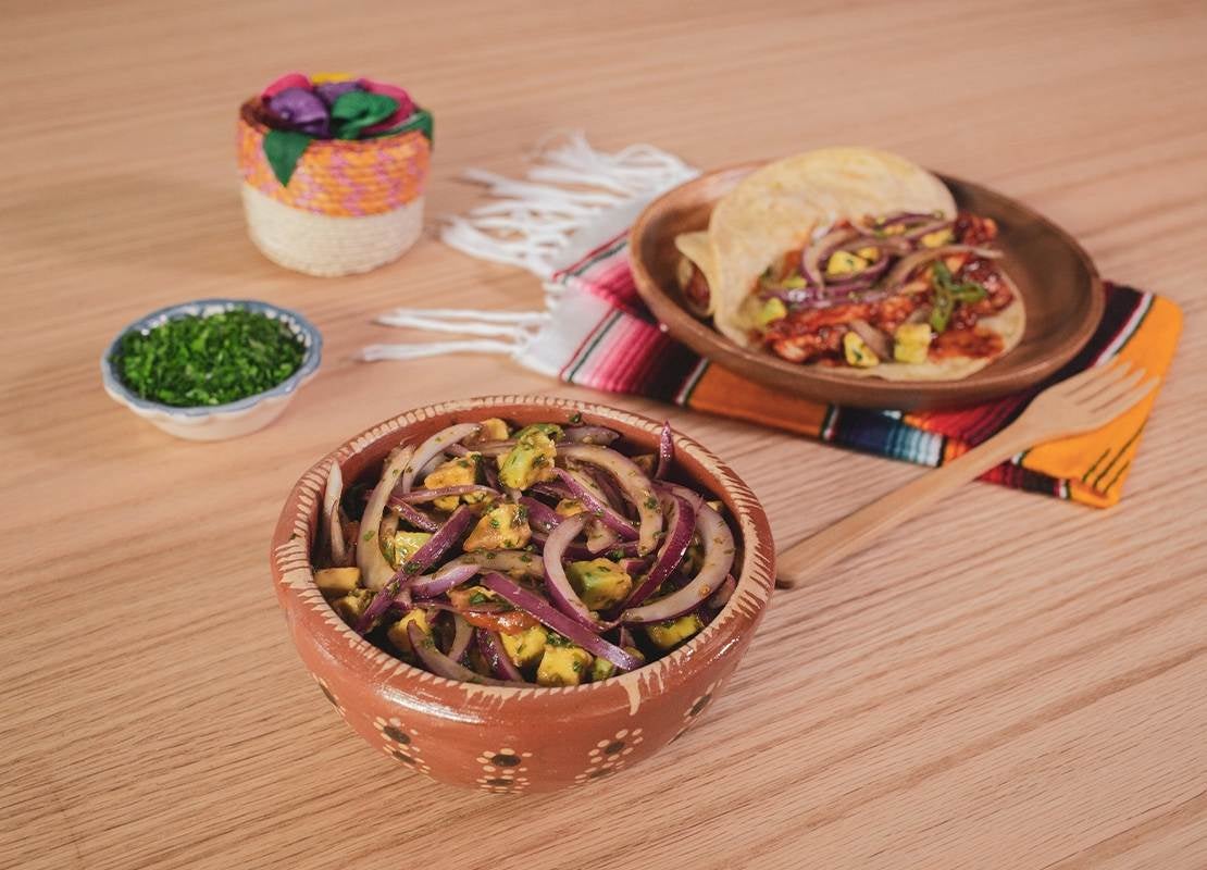 Plato de cebolla morada con piña y especias, acompañado de tacos sobre mantel típico mexicano