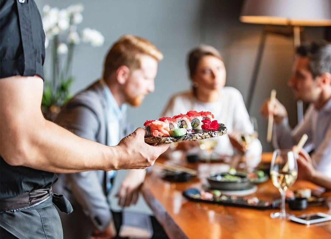 Brazo de mesero sirviendo sushi a un grupo de personas en un restaurante elegante
