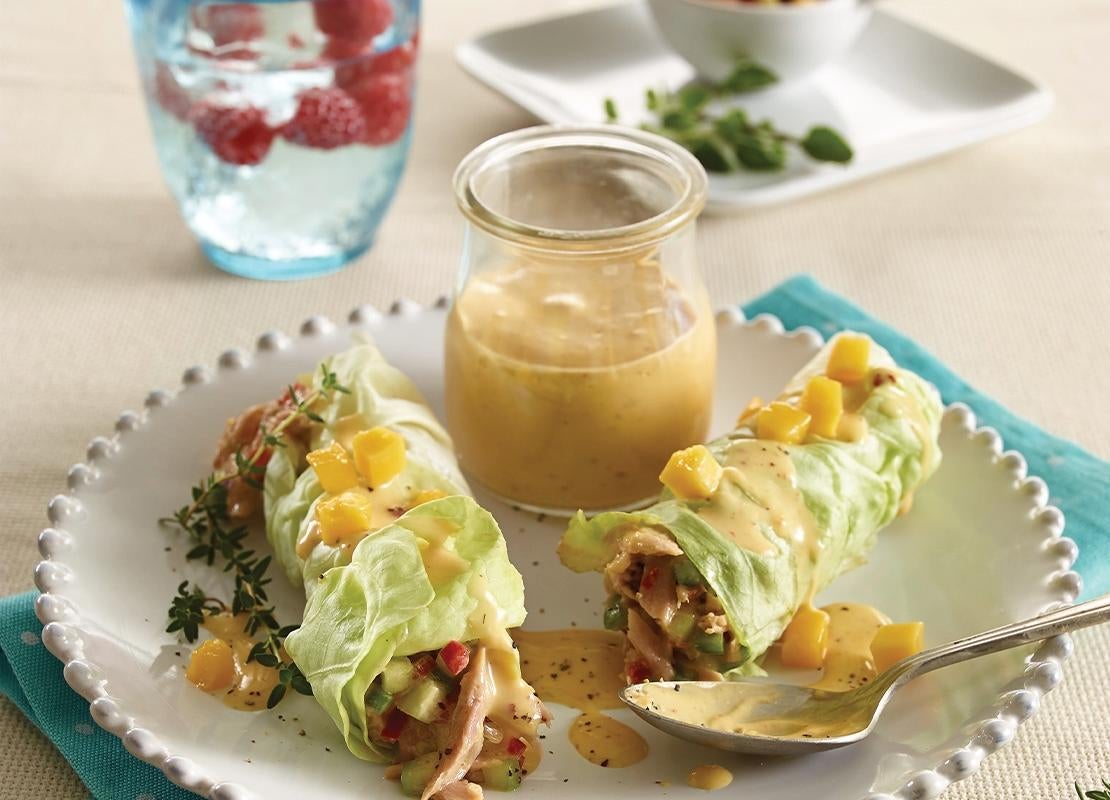 Plato con rollos primavera envueltos en lechuga y un recipiente con salsa, al fondo agua saborizada