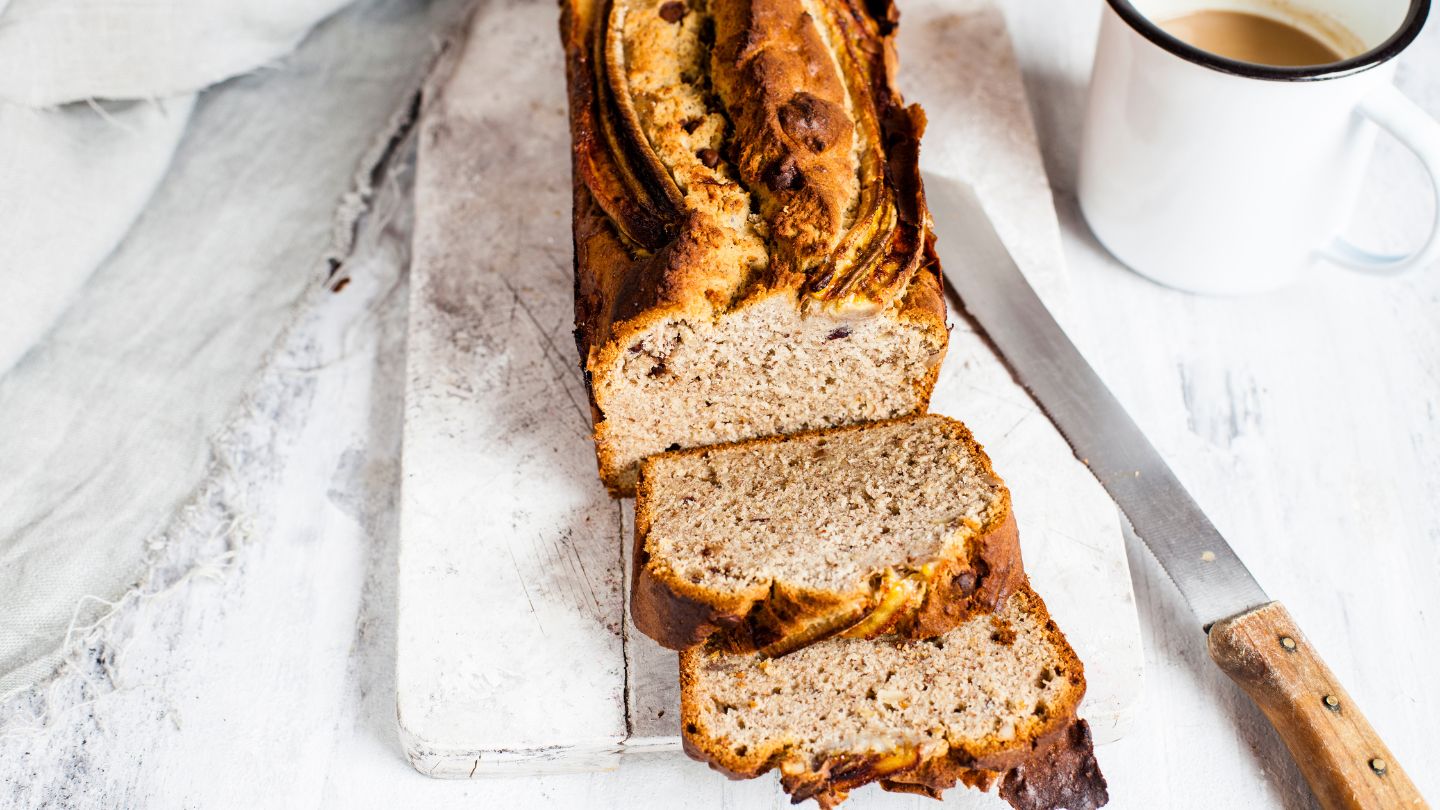 Pan de banano cortado en rebanadas, acompañado de una taza de café sobre fondo claro