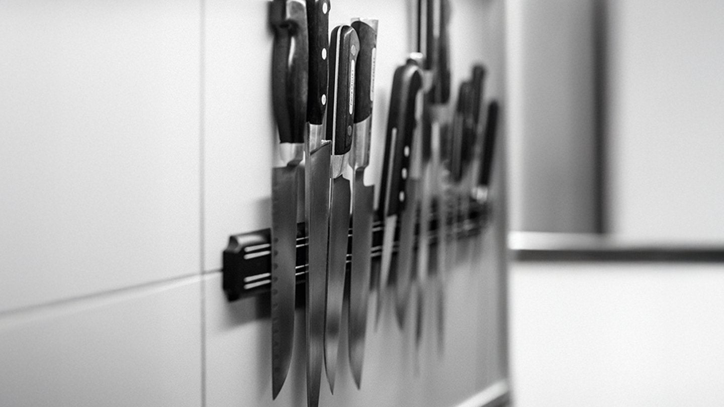 Varios cuchillos de cocina profesionales organizados sobre un soporte magnético en una pared blanca.