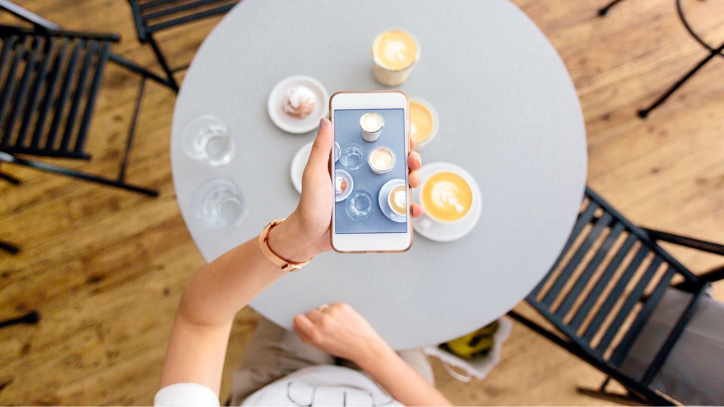 Persona tomando una foto con el celular a varias tazas de café decorado con arte latte sobre una mesa