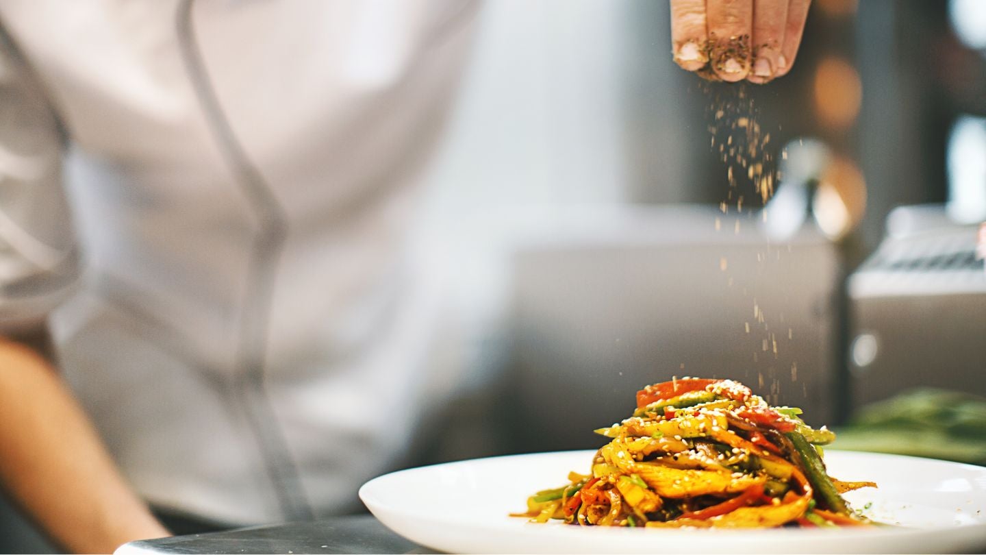 Chef finaliza un plato espolvoreando especias sobre un plato de vegetales salteados