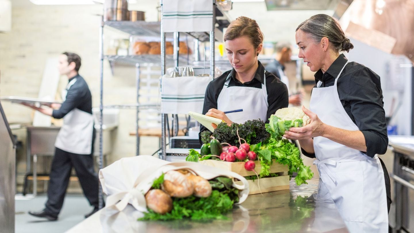 Dos chefs organizan ingredientes frescos, representando prácticas de cocina ecológica en un entorno profesional