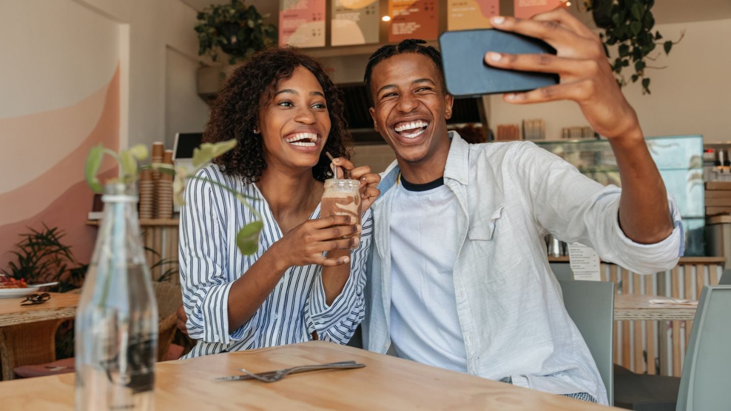 Una pareja sonriente se toma una selfie mientras disfruta una bebida en una cafetería moderna.