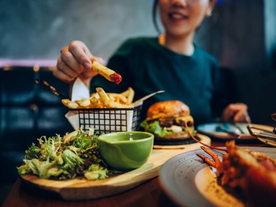 Persona disfrutando un menú casual con papas fritas, ensalada y hamburguesa en un restaurante.