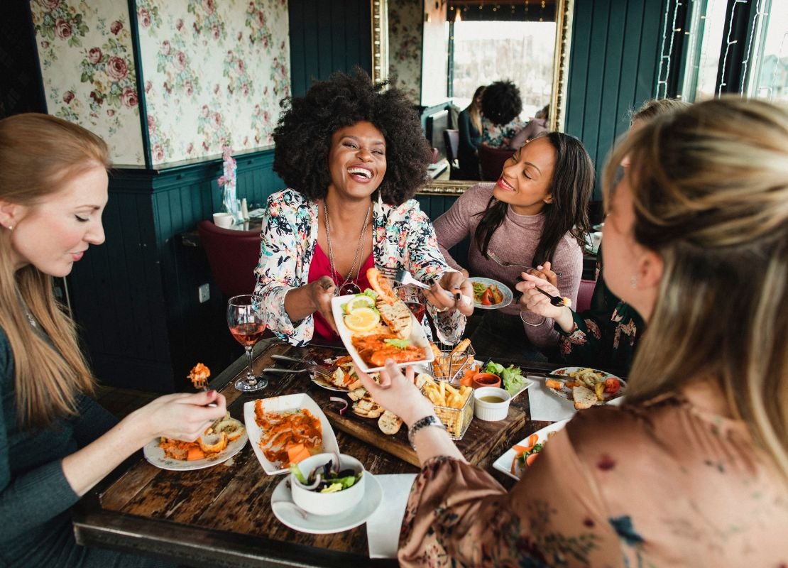Grupo de mujeres comparten un plato de camarones y vino rosado en un restaurante.