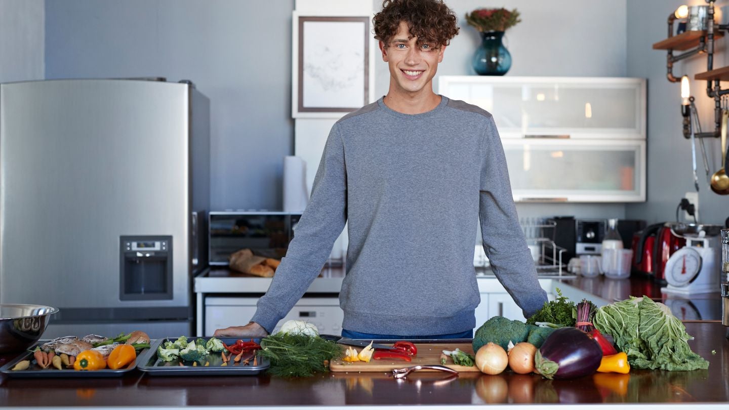 Persona frente a una mesa con vegetales frescos, lista para ofrecer una experiencia culinaria virtual desde la cocina