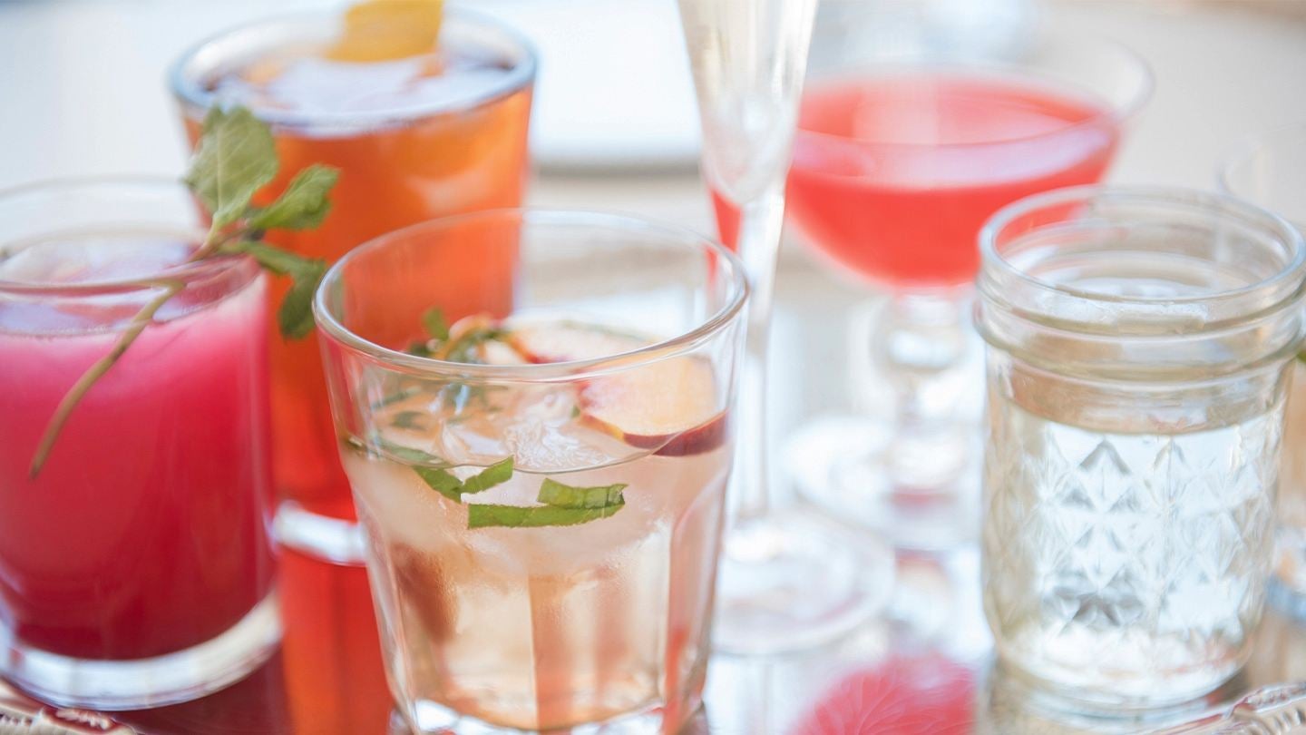 Bandeja con bebidas coloridas, servidas en vasos de cristal distintos estilos y decoradas con hielo, frutas y hierbas