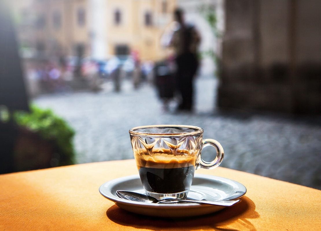 Taza de cristal con espresso sobre plato con cuchara, colocada en una mesa al aire libre
