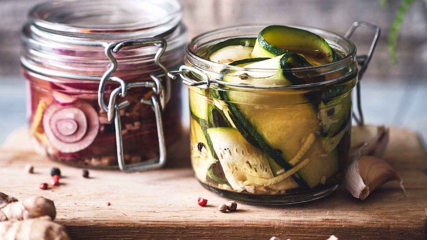 Dos frascos de cristal con cebolla y pepino fermentado sobre una tabla rodeada de ajos
