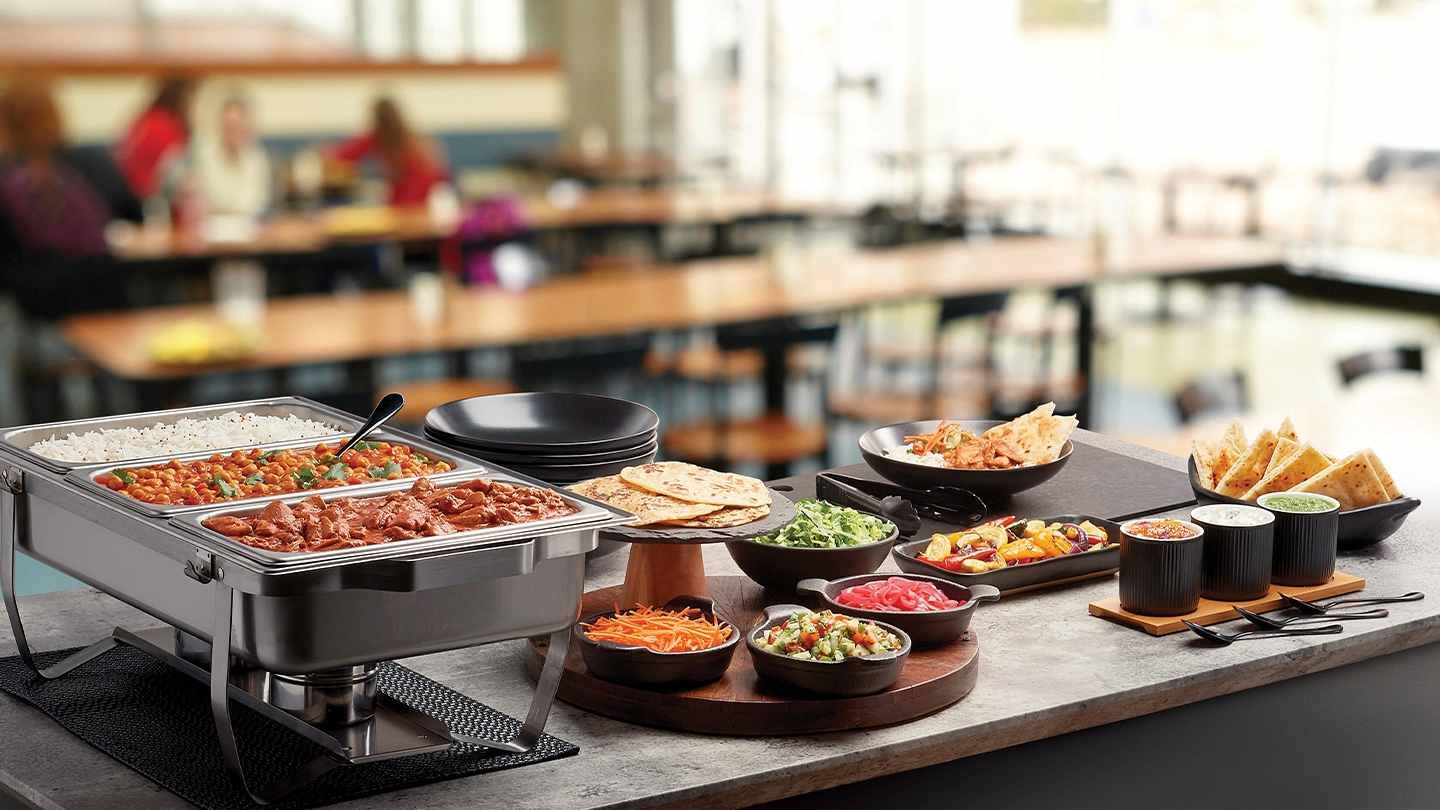 Una food station con diferentes platos, guarniciones y salsas donde los comensales pueden servir su comida.