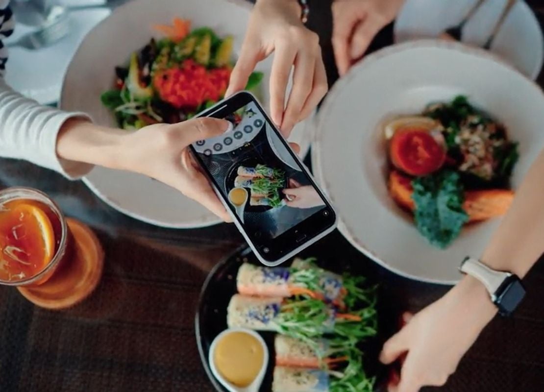 Persona fotografía platos con el celular, mientras otra los organiza sobre la mesa