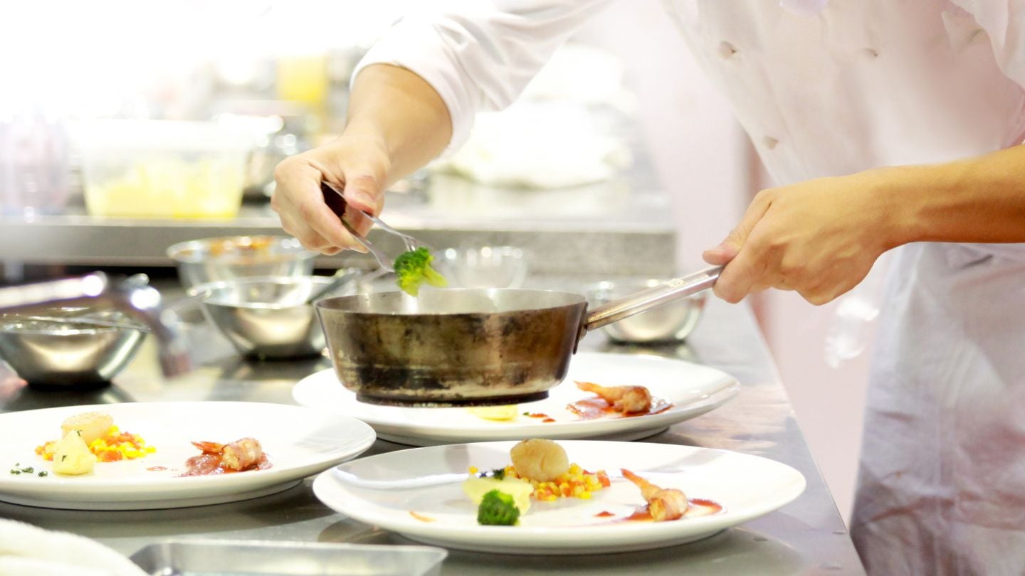 Chef emplatando platos cuidadosamente en cocina profesional, enfoque en calidad tipo Bib Gourmand