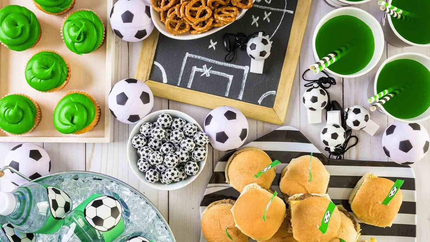 Mesa con snacks y bebidas decoradas con temática de fútbol para servicios de comida en eventos