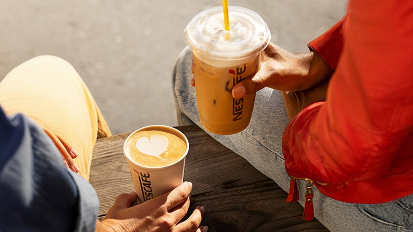 Dos personas sostienen una bebida caliente y una fría servidas en vasos de NESCAFÉ®