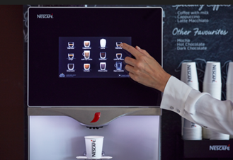 Una máquina NESCAFÉ® dispensa una bebida mientras un usuario selecciona opciones en la pantalla táctil.